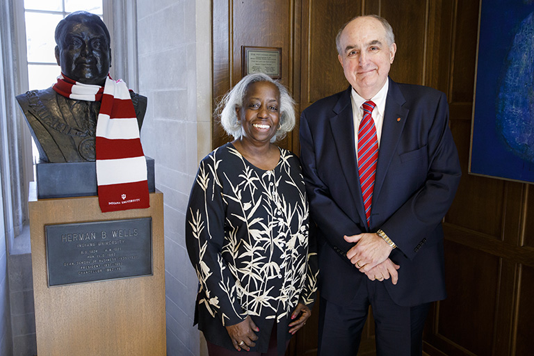 IU alumna Janis Russell and IU President Michael A. McRobbie stand beside a bust of Herman B Well...