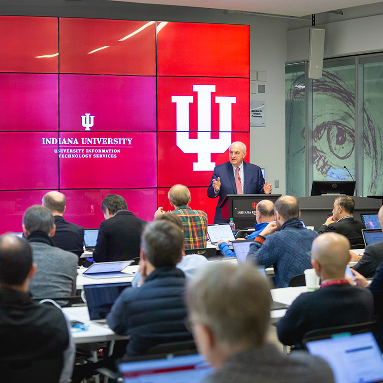 IU President McRobbie speaks in front of a large screen