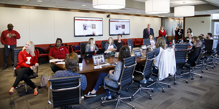 IU President McRobbie and people seated around a long table look up 